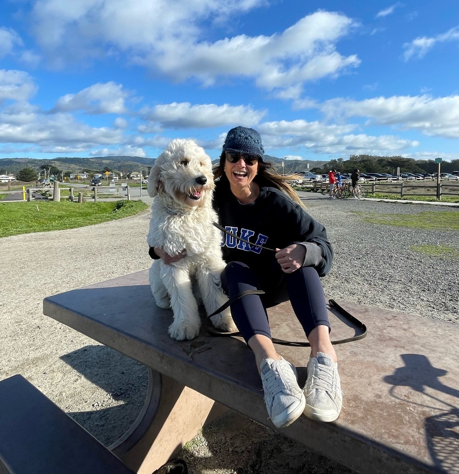 A Caucasian woman sitting on a picnic table with her dog
