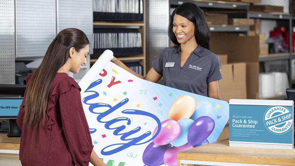 The UPS Store associate displays the customer's new Happy Birthday vinyl banner