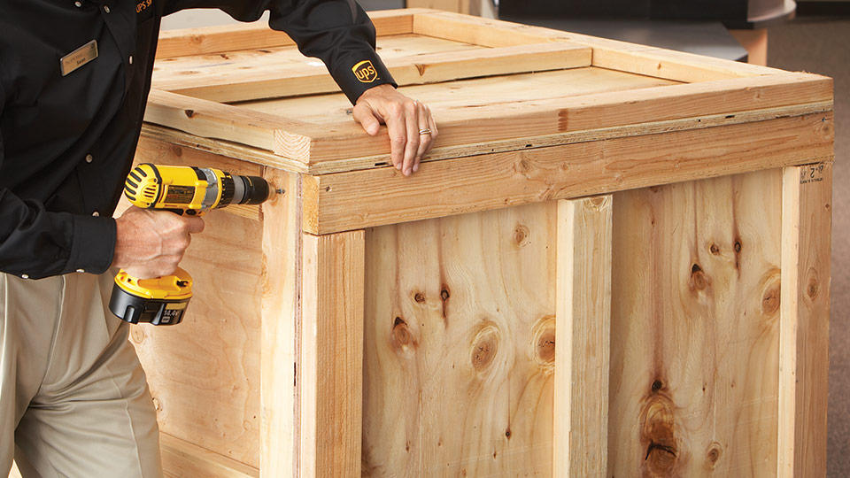 The UPS Store associate closing a custom crate with an electric drill