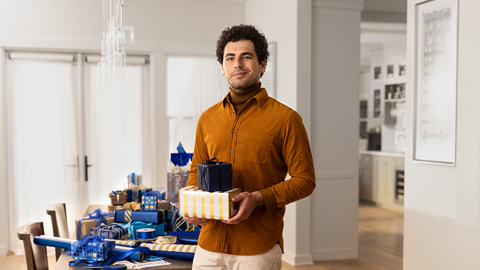 Man holding a wrapped gift in front of a table of gifts.