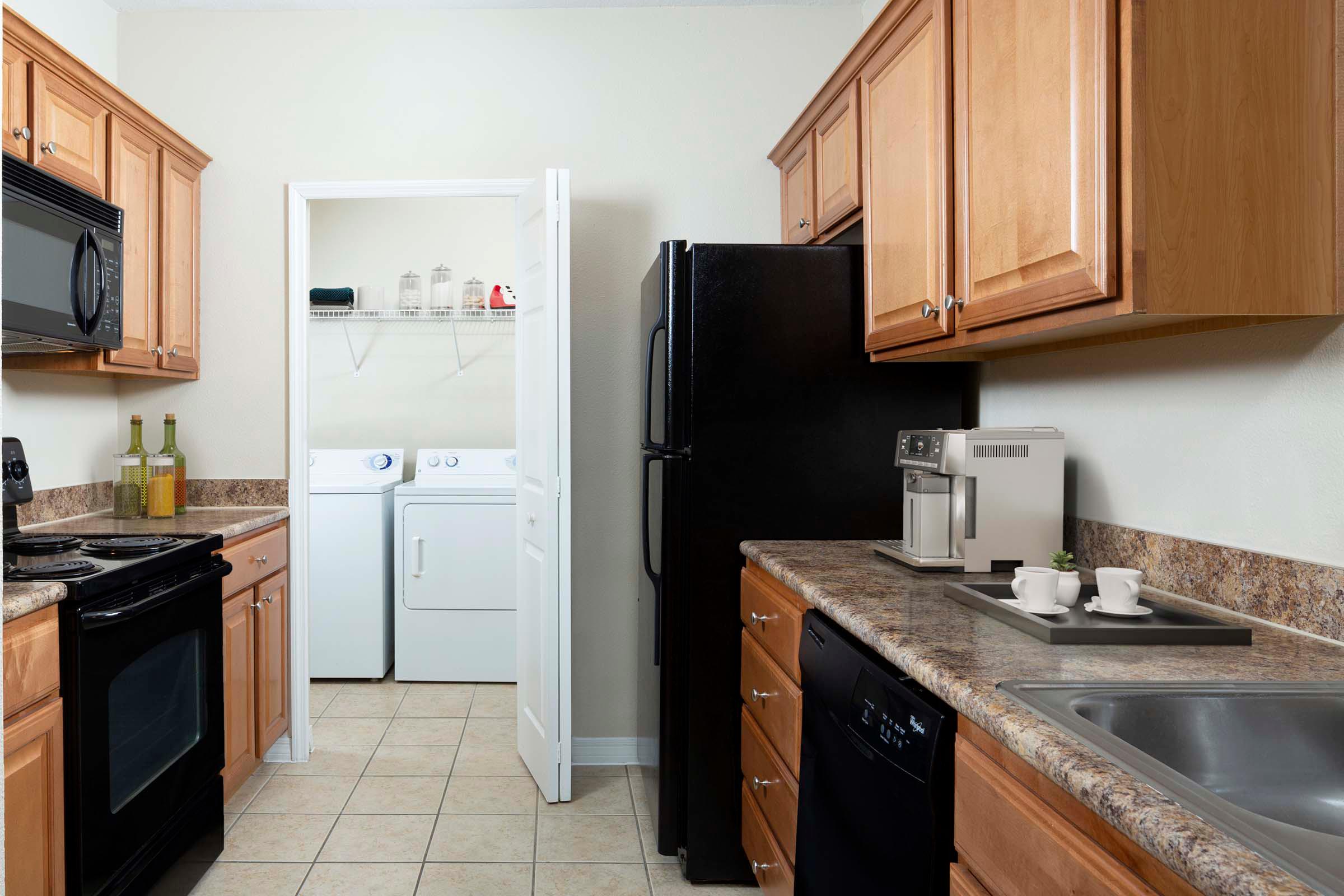 Kitchen with black appliances and tile flooring alongside laundry room with washer and dryer