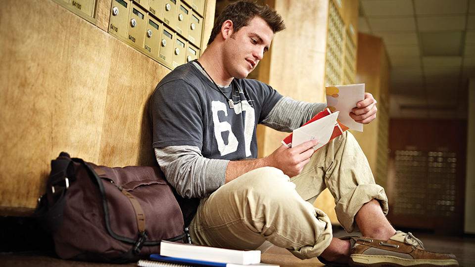 College student reading mail in front of mailboxes