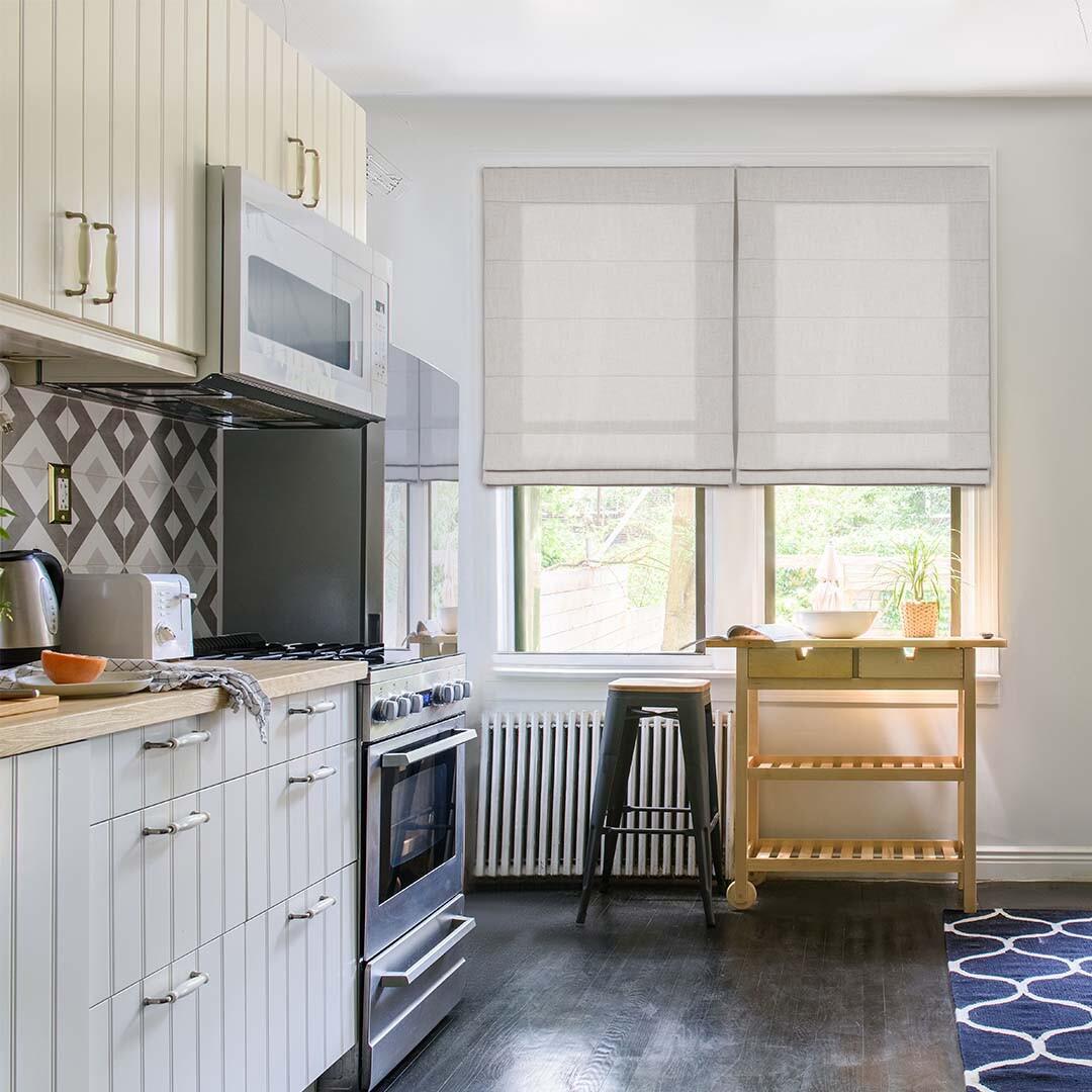 Add a touch of softness to your space with Roman shades. These neutral Roman shades perfectly accent the creamy tones in this kitchen, making for a cohesive design. Contact Budget Blinds to see our full collection of Roman shades.