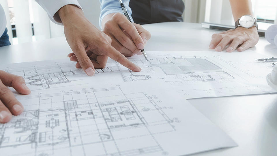 two people standing over and writing on a blueprint