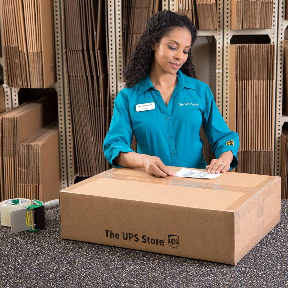 Female The UPS Store clerk placing shipping label on package