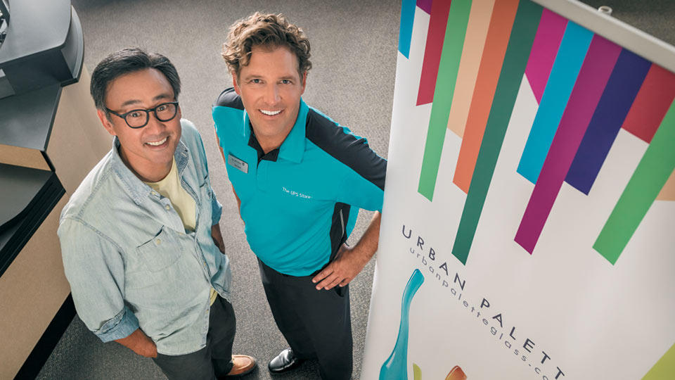 a customer and The UPS Store associate smiling next to a retractable banner