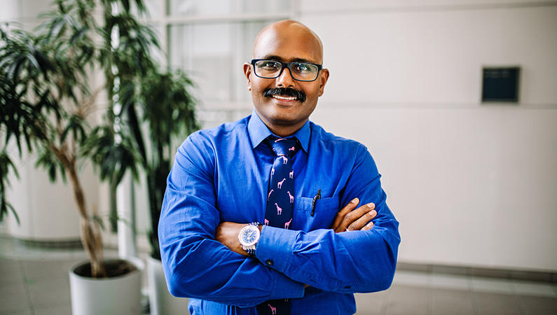 Man smiling wearing glasses posing with arms folded in naturally lit atrium area