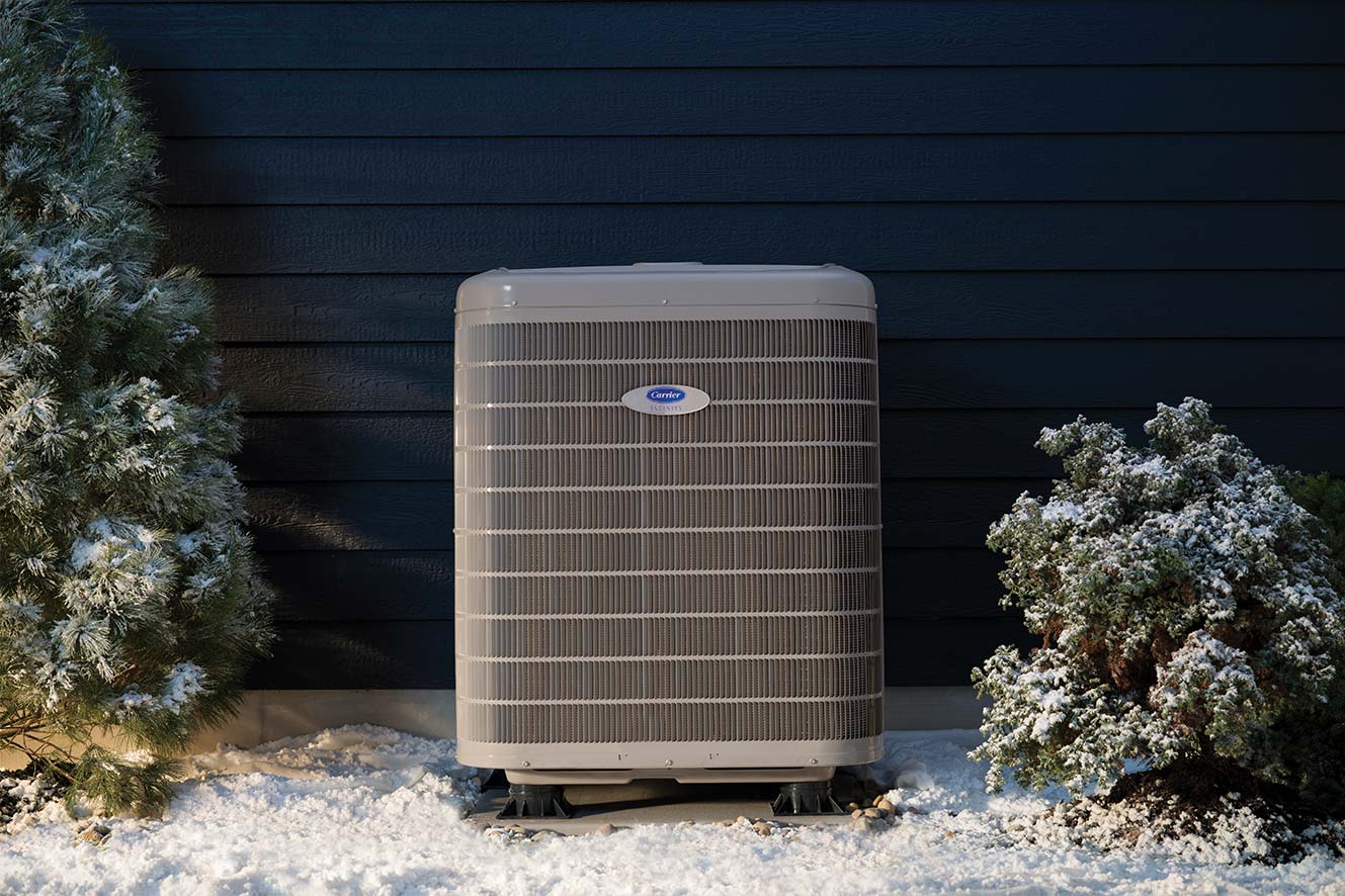 An Infinity heat pump installed outside a home in winter snow