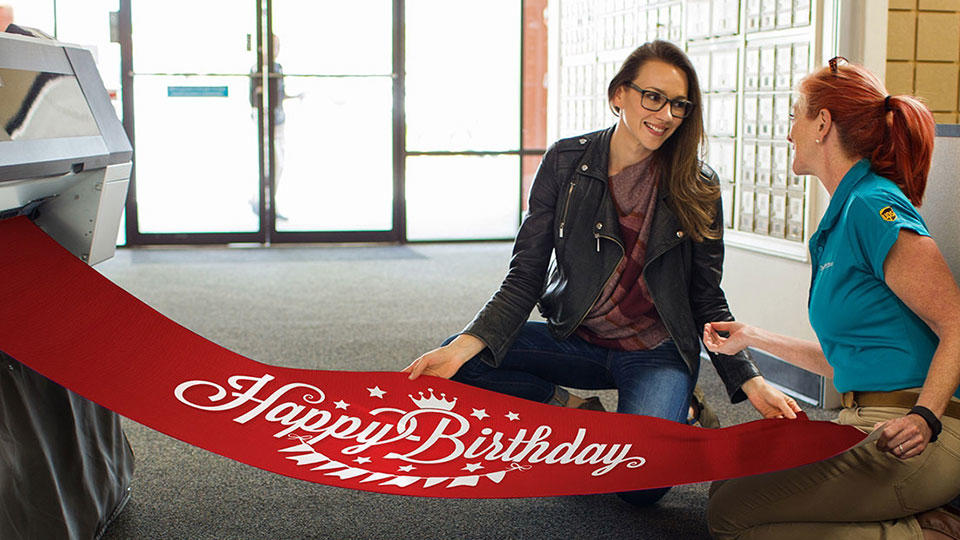 Employee and customer inspecting red birthday banner with white text