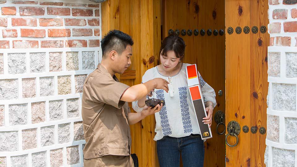 Un repartidor de UPS entrega un paquete a una mujer de pie en un portal de ladrillo.