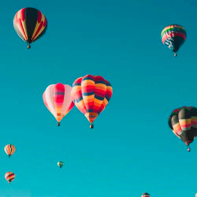 A sky filled with colorful hot air balloons against a clear blue backdrop, creating a vibrant and joyful scene. Patterns and colors vary among the balloons.
