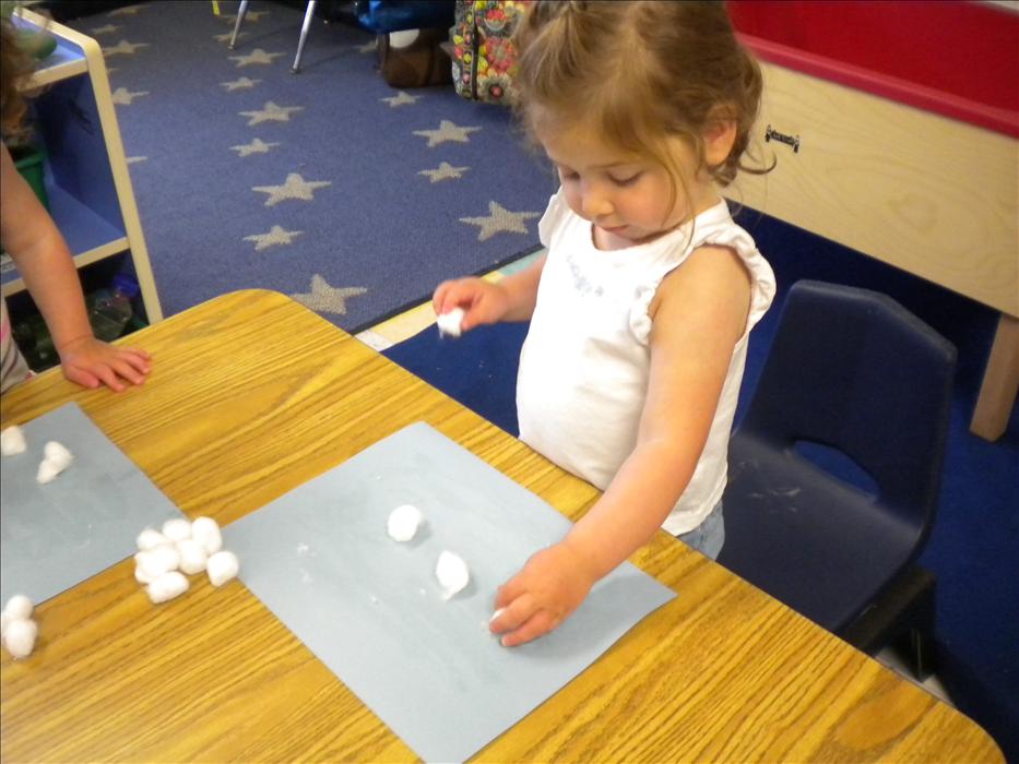 The toddlers are talking about the weather. After a weather discussion, our friends worked on creating their our cloudy sky with cotton balls just as you see Juliette working so hard on completing.