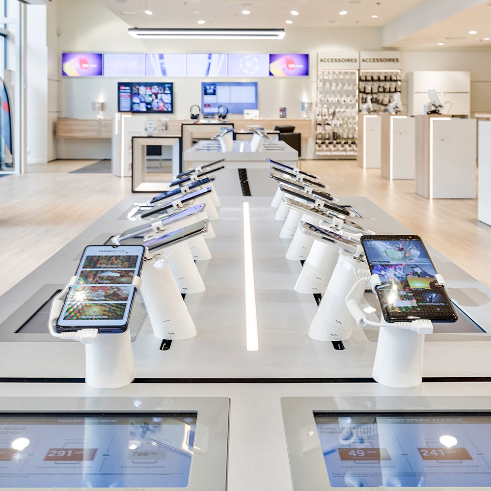 Des iPads et smartphones sont disposés sur des présentoirs blancs, eux mêmes posés sur une grande table à l'intérieur d'un showroom SFR