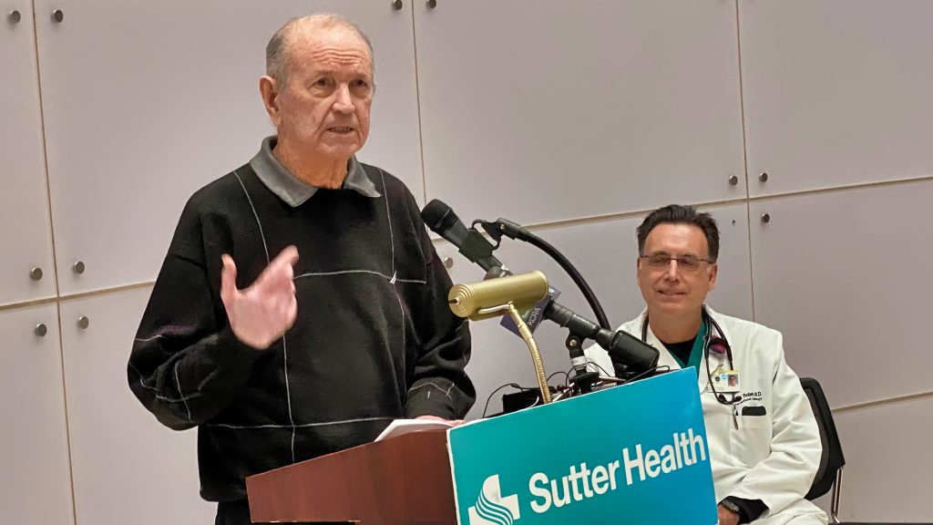 Man speaking at podium with other many looking at him.