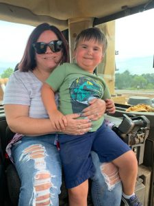 Caucasian mother sits with young son in her lap in a large motorized touring vehicle.