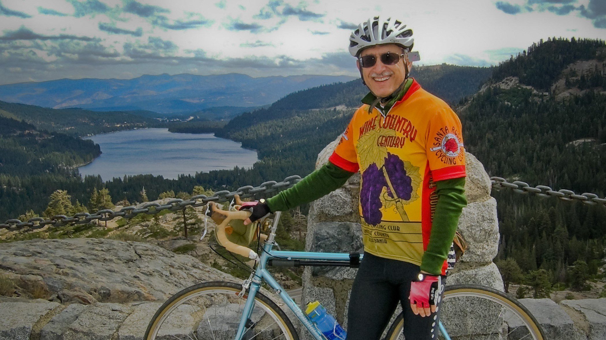 Man with bike helmet with bicycle and lake behind him