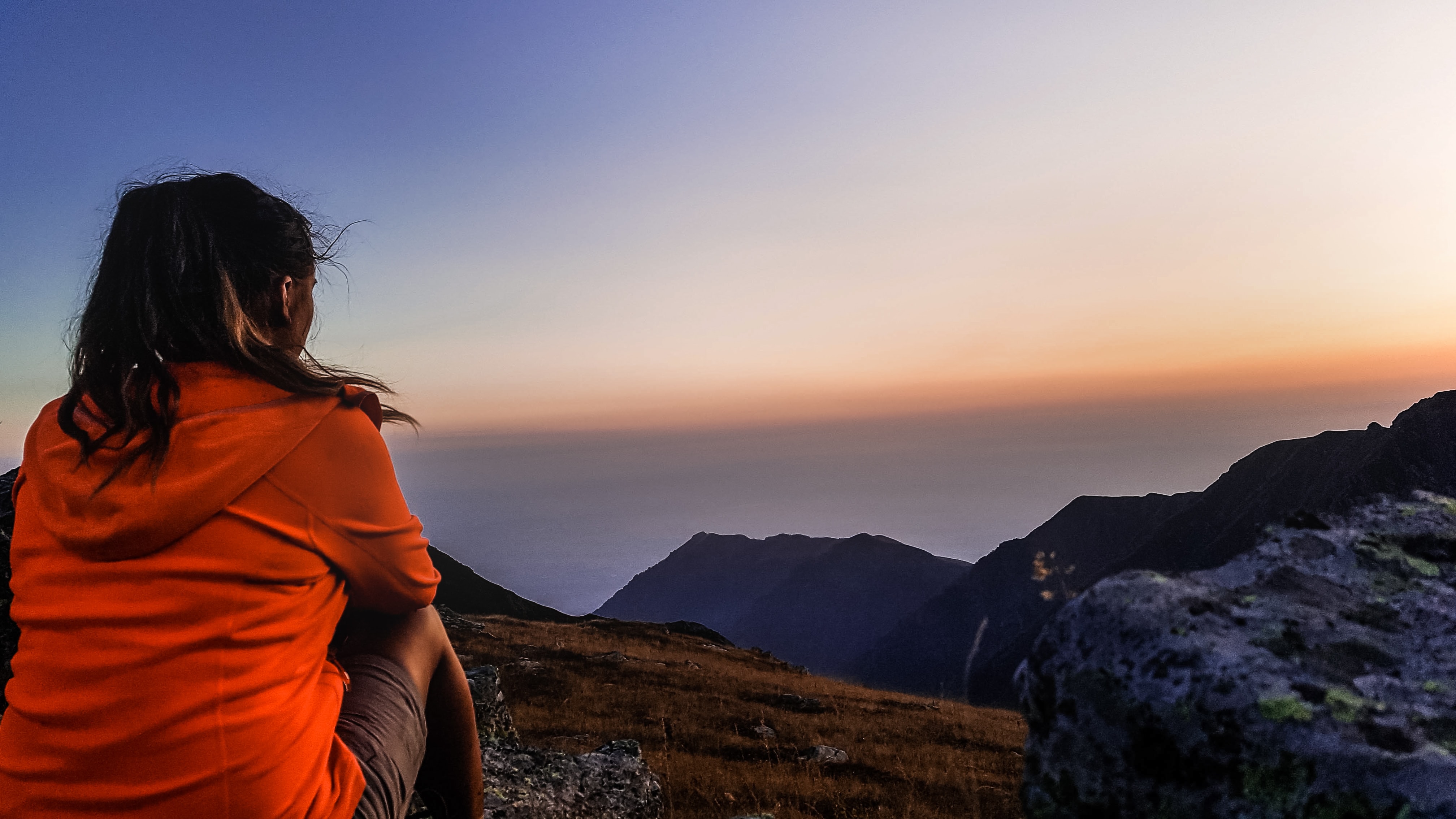 Girl sitting on mountain overlooking sky.