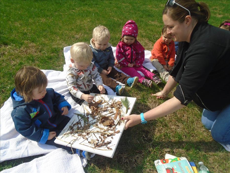 Miss Karla is teaching her Discovery Preschool class that they can use sticks, leaves and rocks to create an art project outdoors!