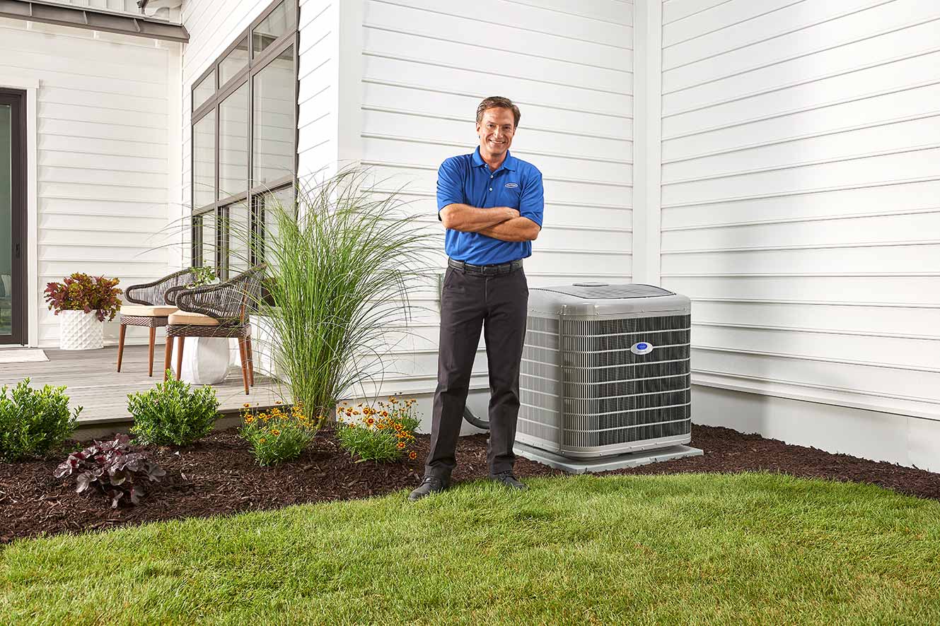 A Carrier dealer standing next to a heat pump after servicing it