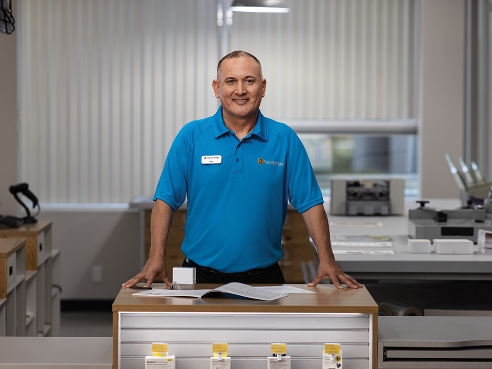 The UPS Store associate standing behind a table with documents and a stamp