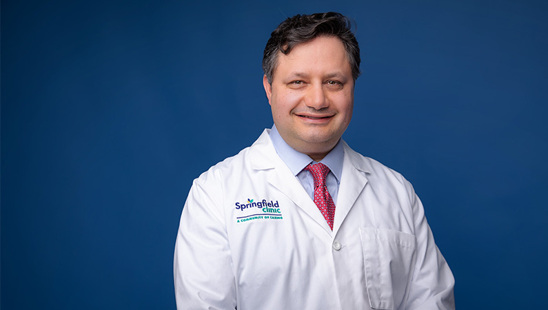 Male radiation oncologist in white doctor coat smiling in front of a photo backdrop.