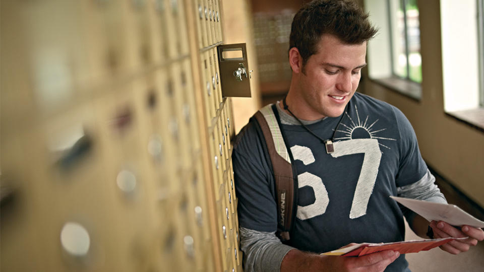 College student reading mail in front of mailboxes