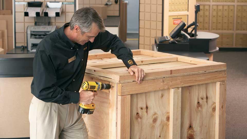 El asociado de The UPS Store cierra una caja personalizada con un taladro eléctrico.