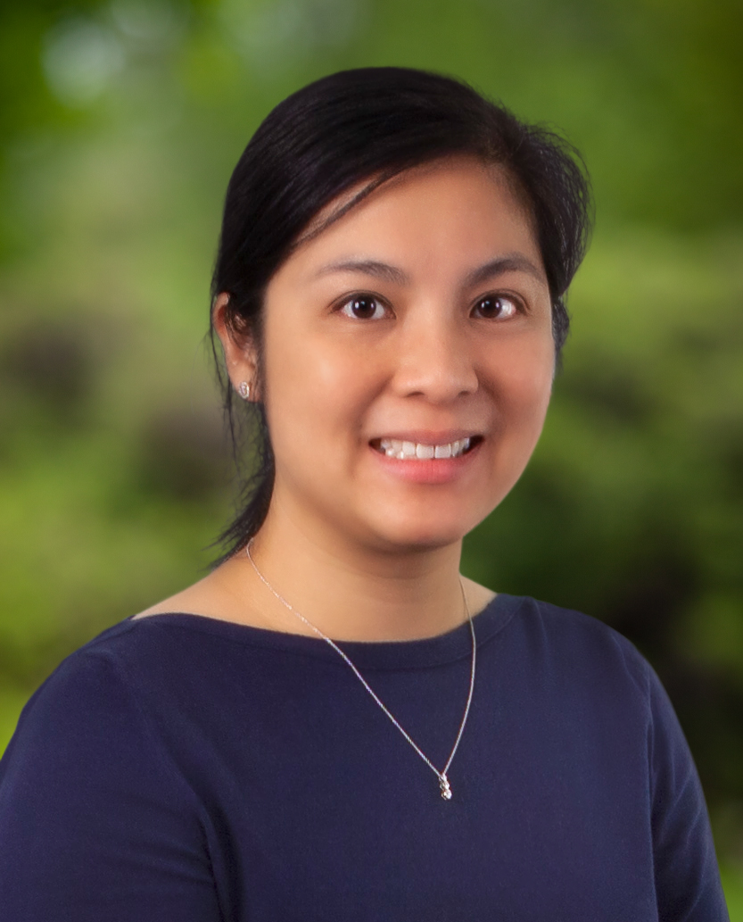 An Asian woman wearing a blue shirt with a gold necklace smiles.