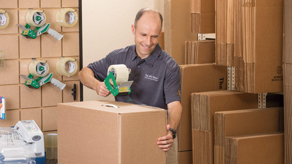 a smiling associate tapes shut a shipping box at The UPS Store