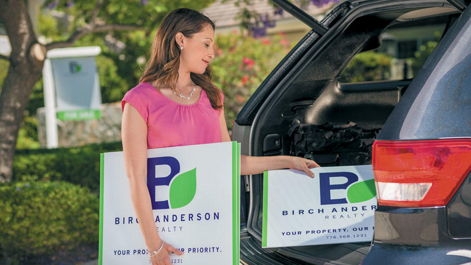 Female loading lawn signs into trunk of car