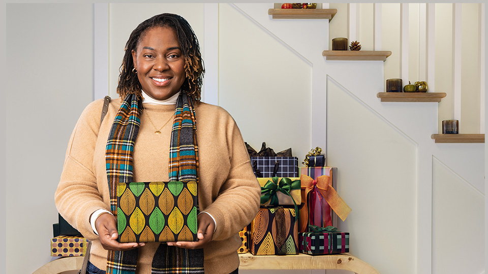 Woman holding a wrapped gift in front of a table of gifts. ​