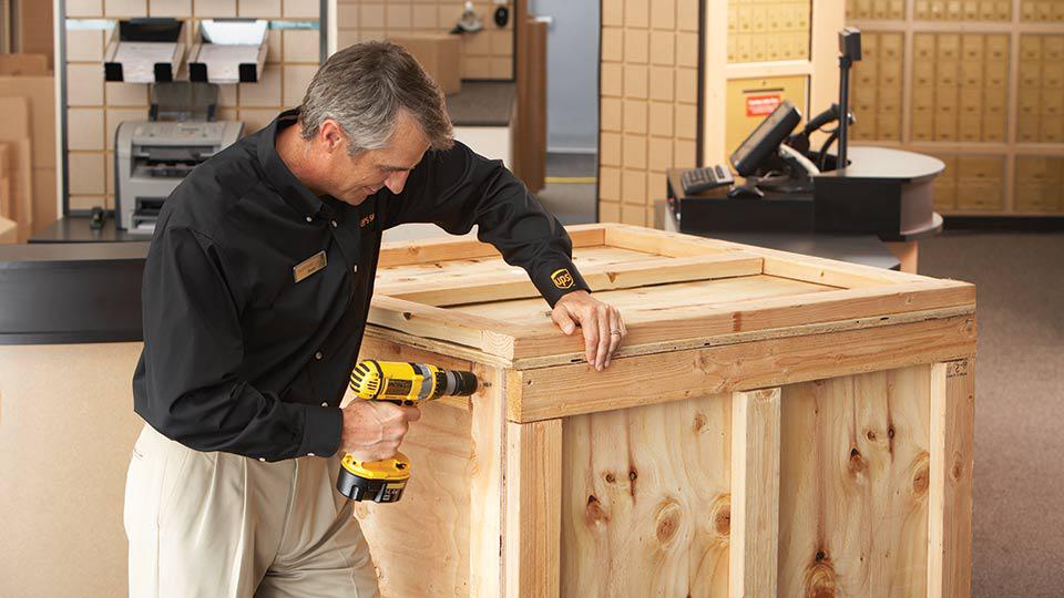 The UPS Store associate closing a custom crate with an electric drill