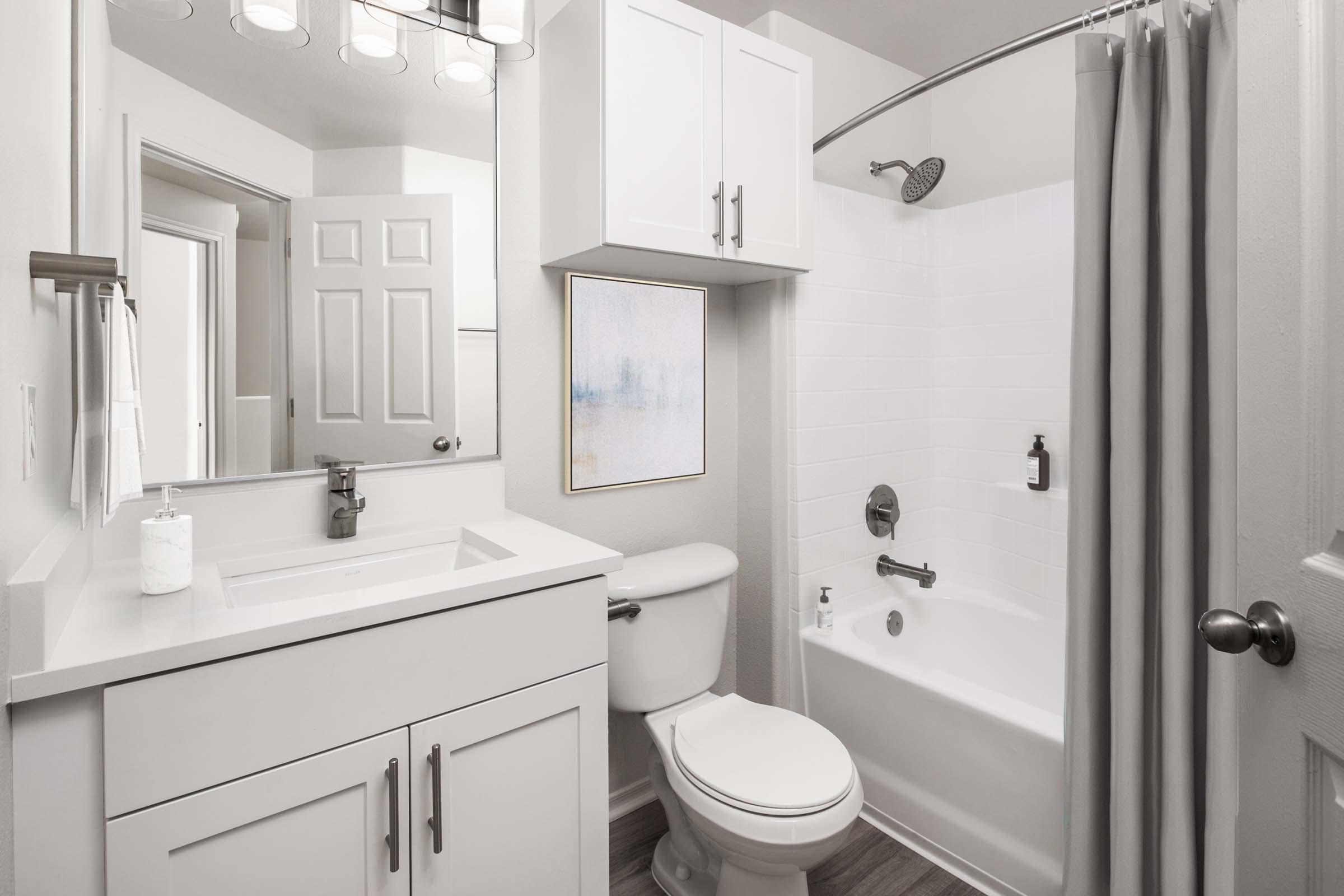 Bathroom with white shaker cabinets, white quartz countertops, brushed nickel fixtures and curved shower rod