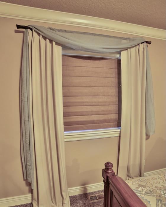 Draperies and a Custom Valance add a unique style to these Roman Shades in a bedroom in Kuna, ID. Pairing coverings is a great way to create a one-of-a-kind look.  BudgetBlindsBoise  CustomDraperies  RomanShades  CustomValance  FreeConsultation