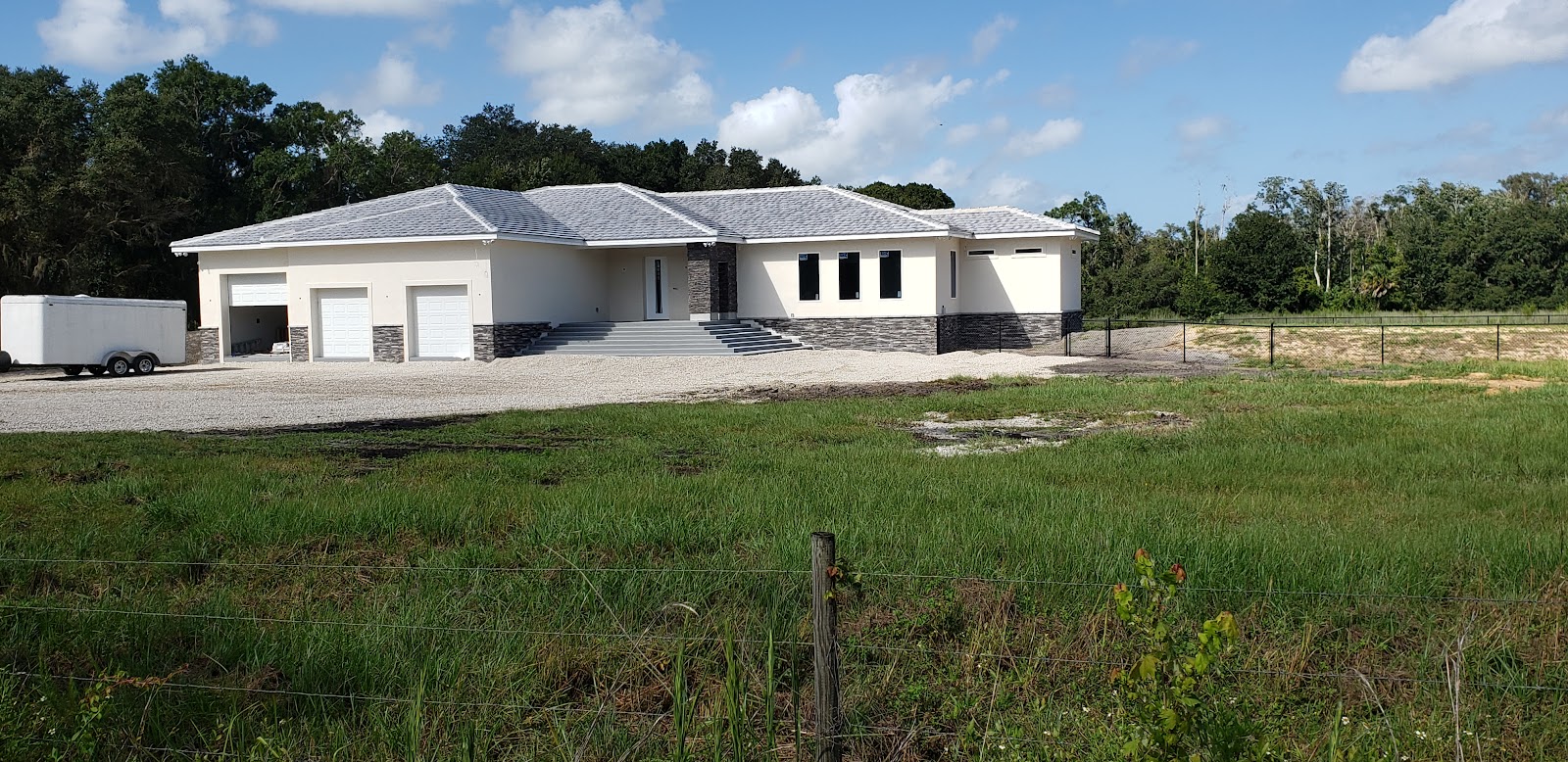 A newly constructed single-story house with a light-colored exterior and a gray roof, situated on a  