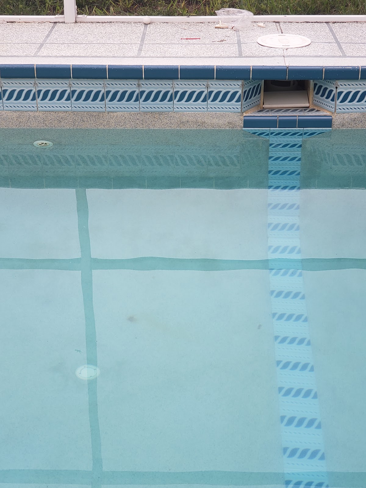 Close-up of a swimming pool wall with waterline tile, clear water, and a built-in pool fitting.