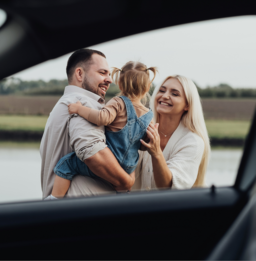 A smiling family seen from the side window of a car.