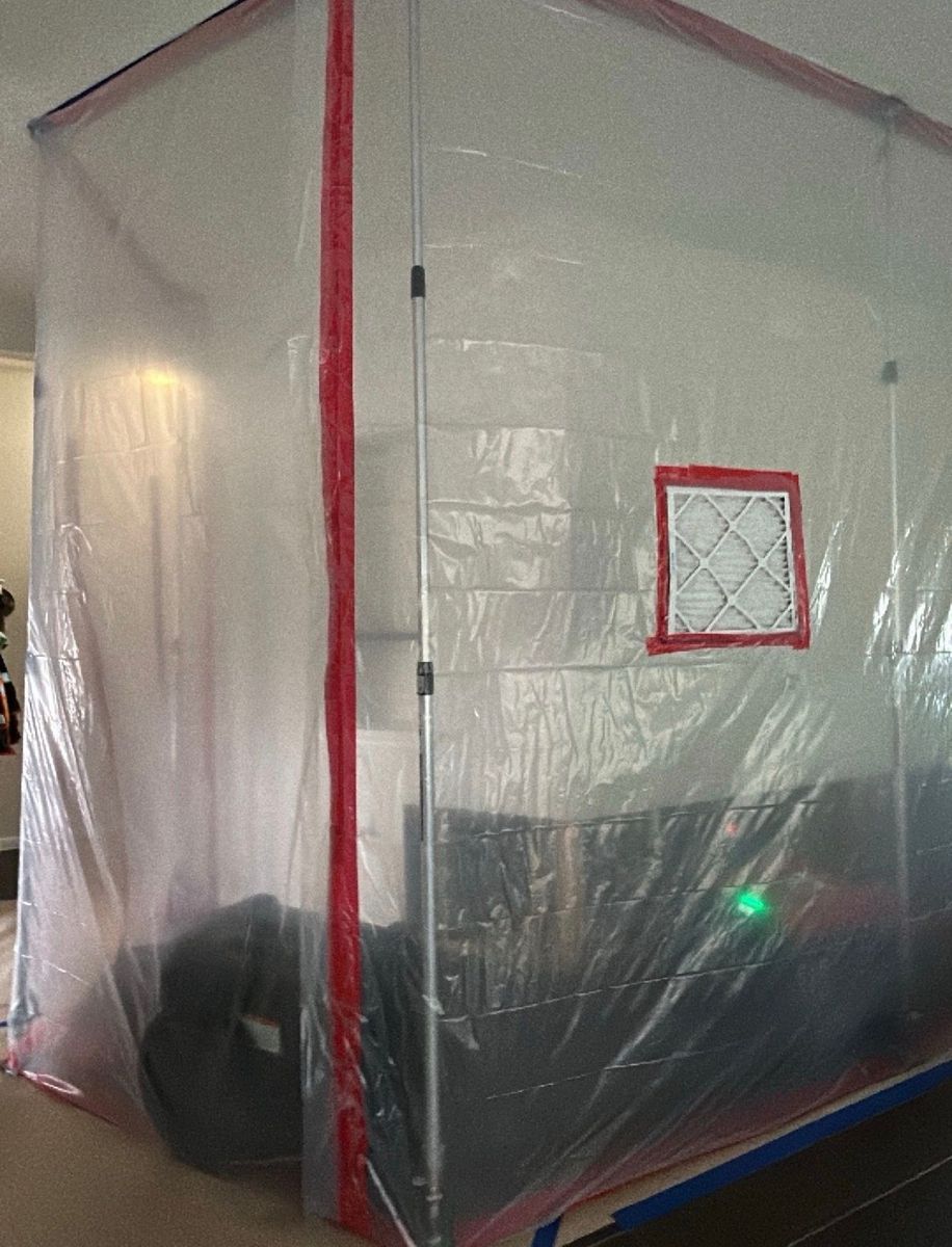 A temporary plastic containment enclosure surrounds part of a residential interior, sealed with red  
