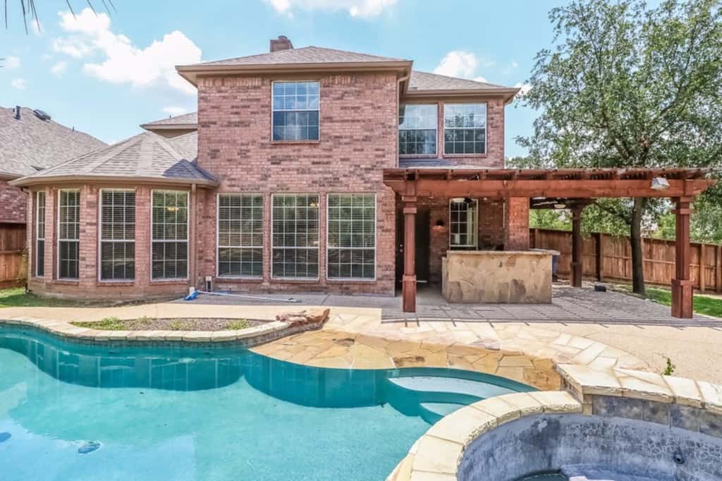 Beautiful back of home shot with oversized windows, pool and pergola at Invitation Homes Dallas.