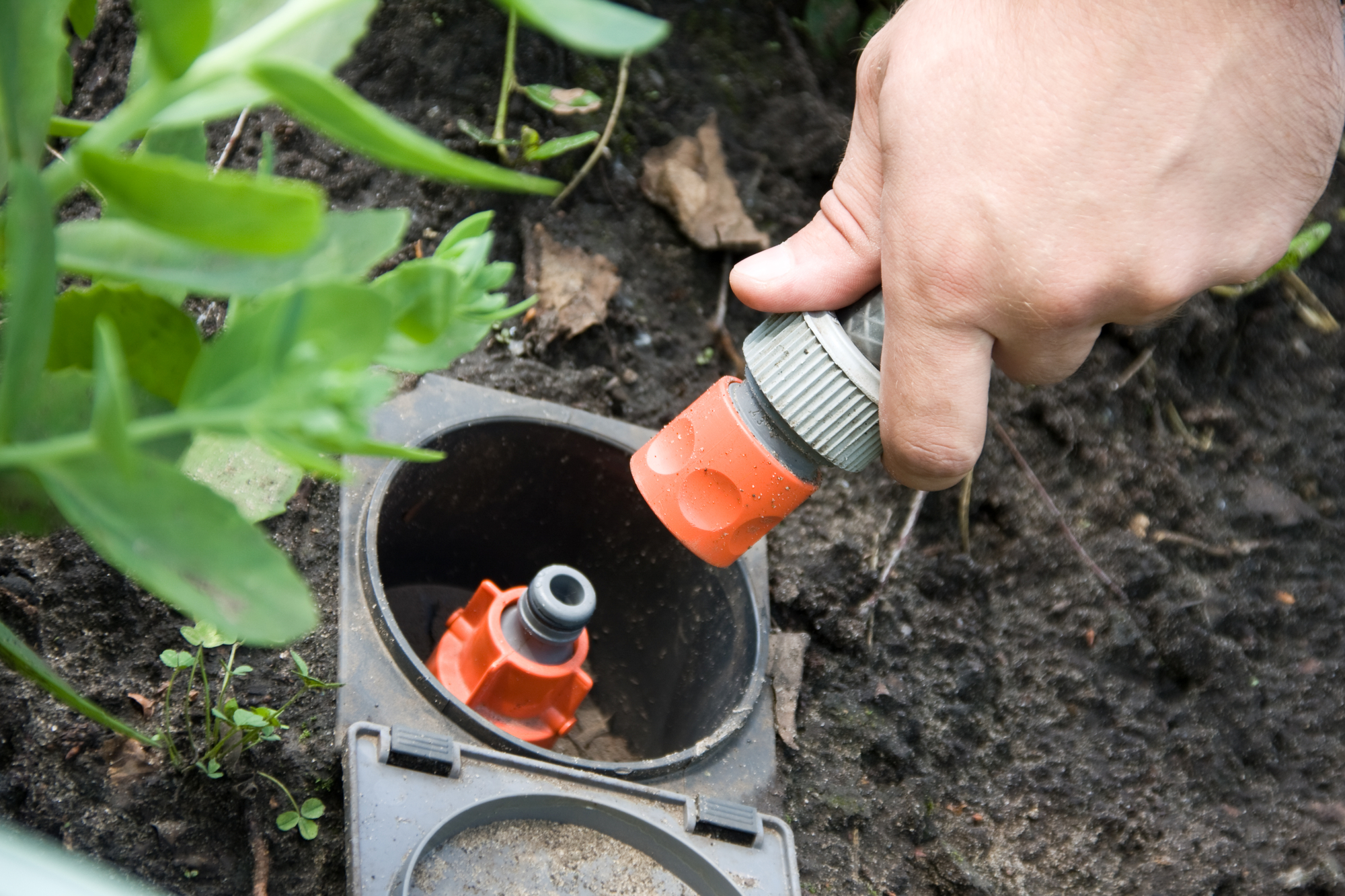 A technician servicing an underground irrigation system valve box to adjust water flow or repair connections.