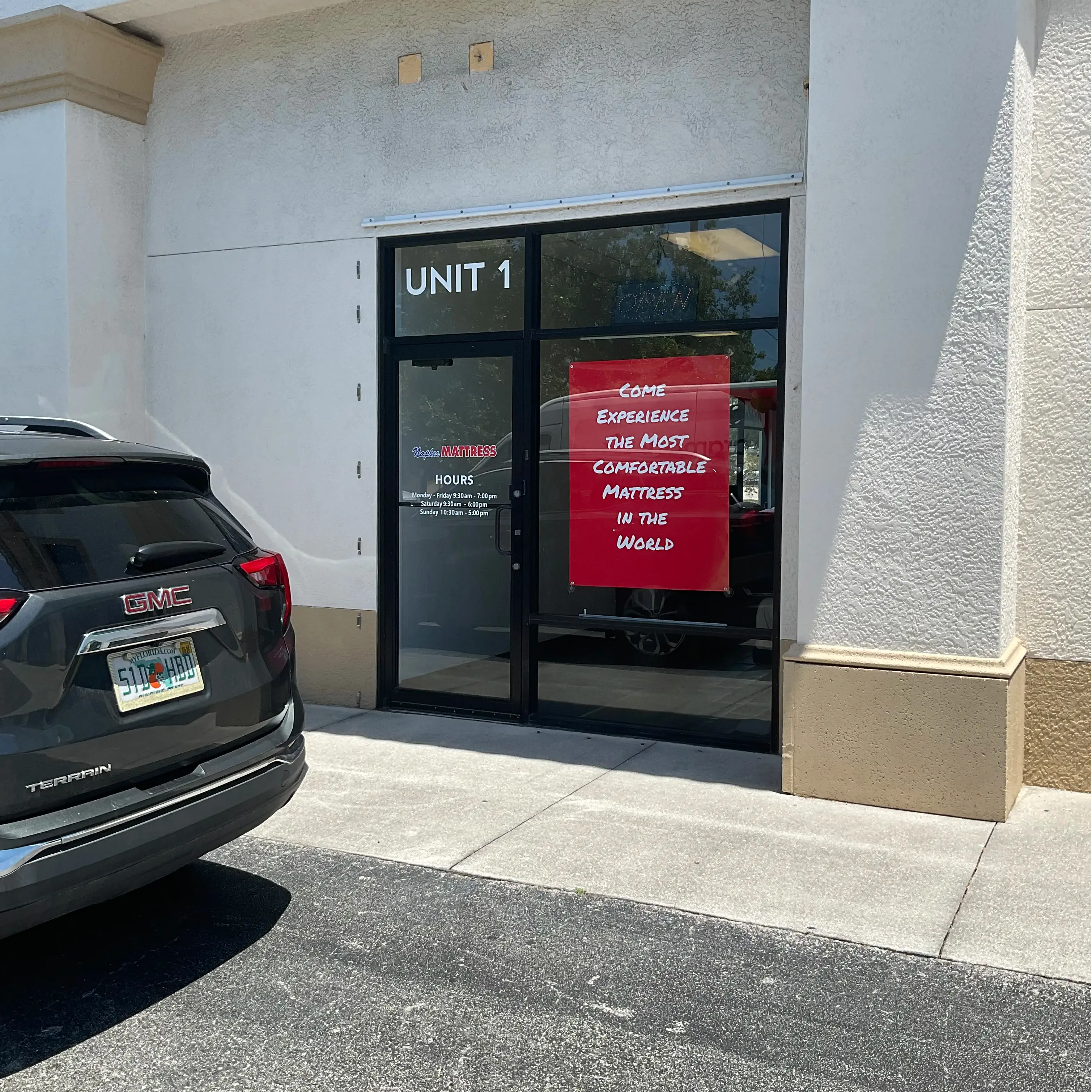 Side entrance to Naples Mattress North at Unit 1, with store information displayed on the glass door.