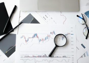 A magnifying glass, glasses, writing tools, and a piece of paper displaying a graph scattered on the top of a table.