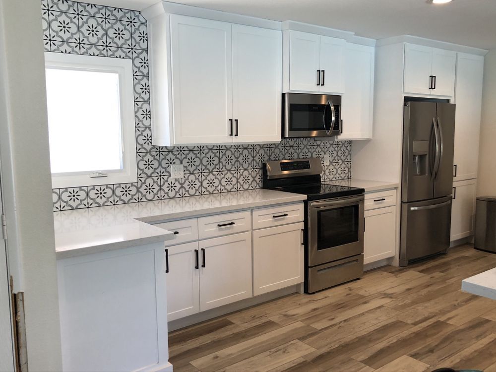 A spacious, modern kitchen features white shaker-style cabinets, light wood-look flooring, and a uni 