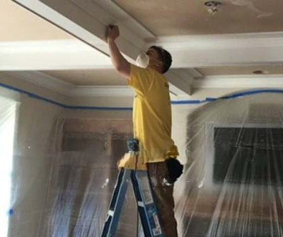 Professional painter working from ladder while preparing and painting ceiling surfaces, protecting s 
