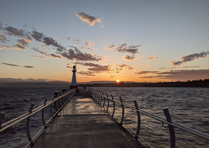 A scenic pier with lighthouse at sunset.