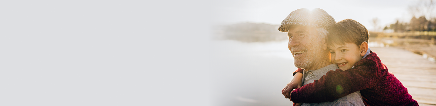 A grandfather smiling while carrying his grandson on his back.