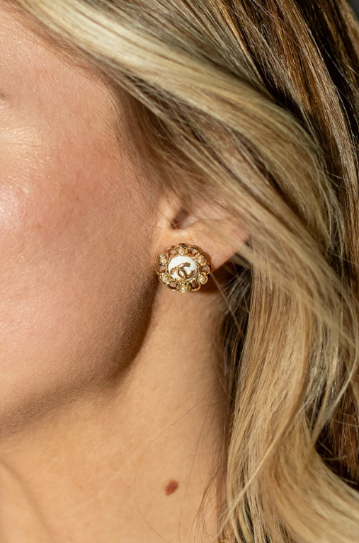 A floral gold-toned earring with a white center, interlocking logo, and sparkling accents adds an elegant polished touch. Explore statement earrings at Eliana Curated in Old Town Alexandria, Virginia.