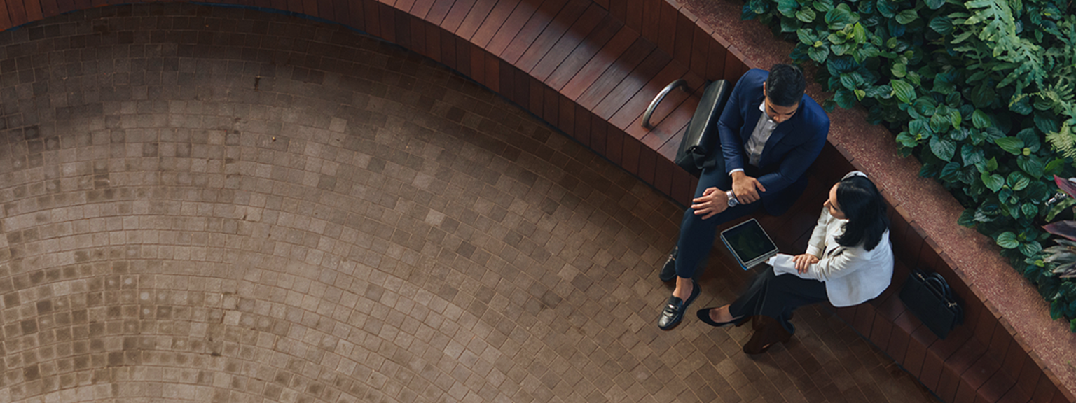 Top-down view of two professionals talking while on a park bench.