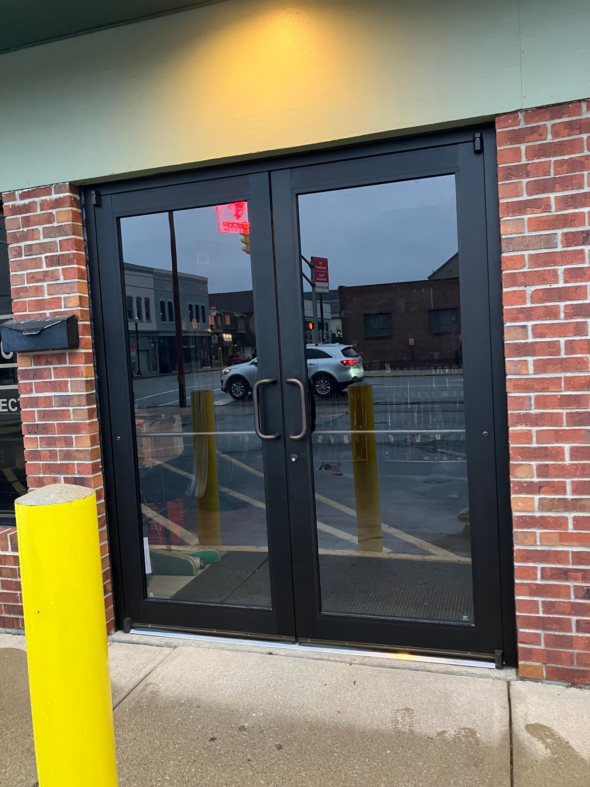 Commercial double glass entry doors with black frames installed in a brick building, reflecting the surrounding street and providing a durable, modern entrance for businesses and customers today entrance doors.