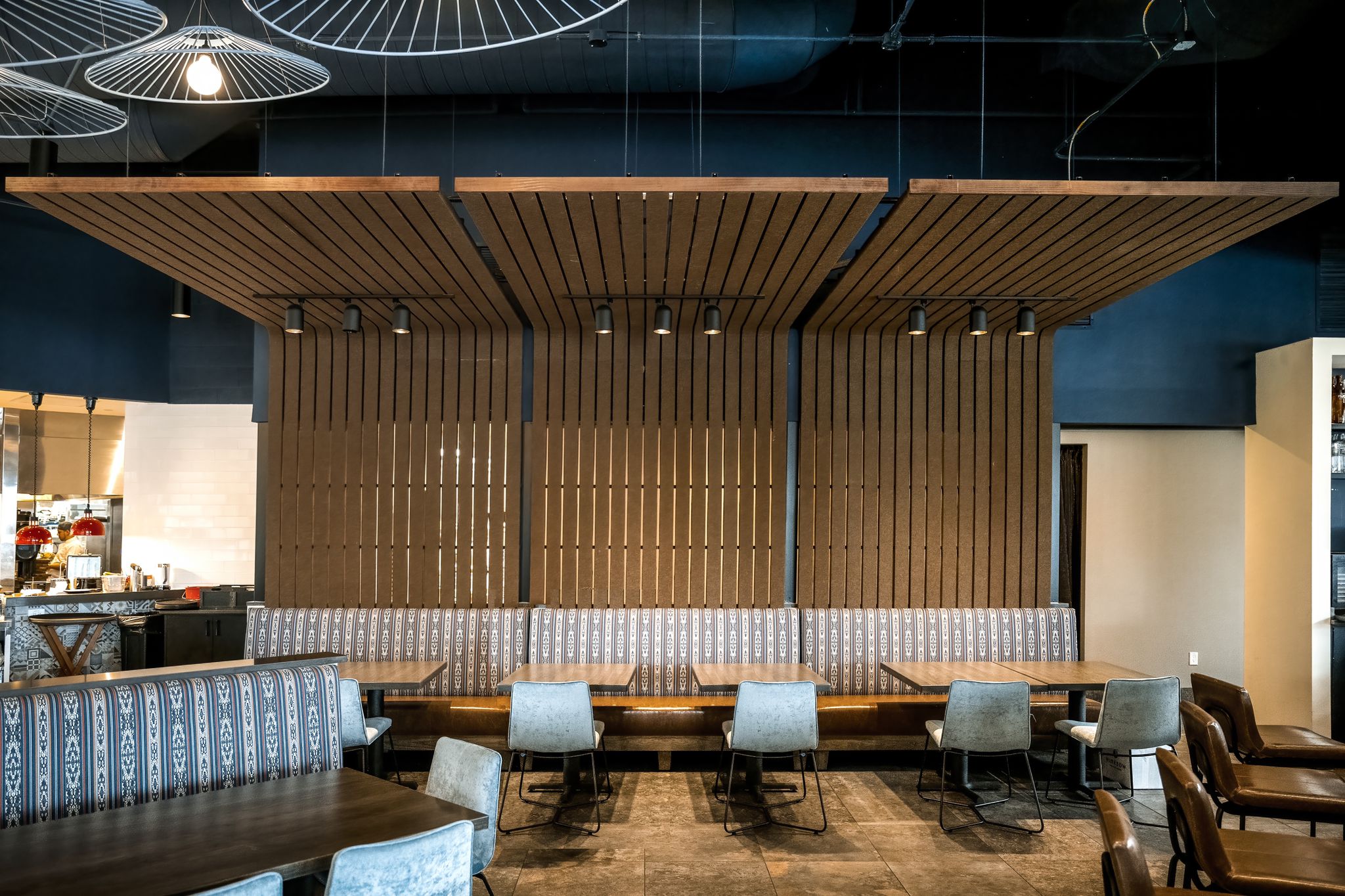 The dining area showcases clean and elegant lines with a warm ambiance created by wooden accents and neutral-colored furnishings. The lighting design adds a contemporary touch, and the open kitchen is visible in the background.